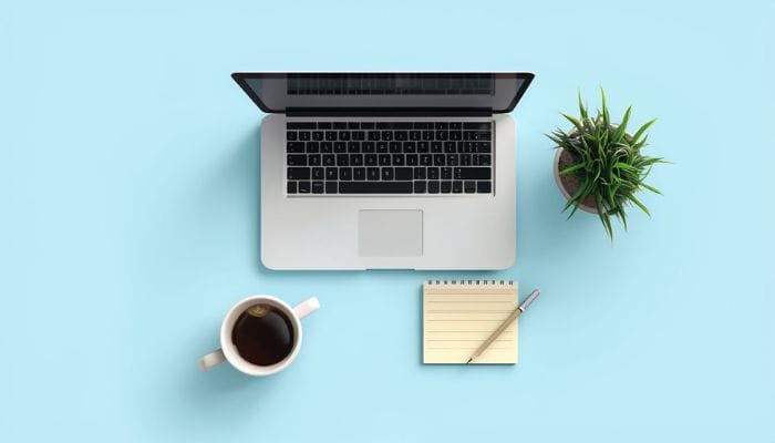 workspace scene featuring an open laptop with a sleek design, resting on a soft blue surface. Include a white coffee mug filled with dark coffee