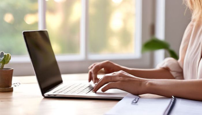 a woman typing on a laptop in a sunlit room